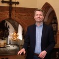 Ein Mann in Jackett und Hemd steht auf der Empore einer Kirche. Im Hintergrund Kreuz und Altar