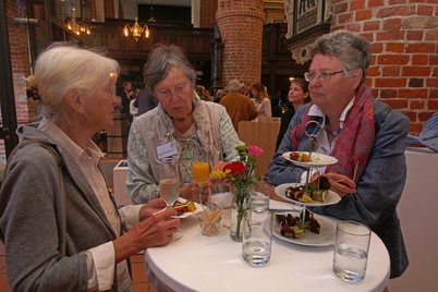 Drei Frauen unterhalten sich an einem Stehtisch mit Blumen und Essen