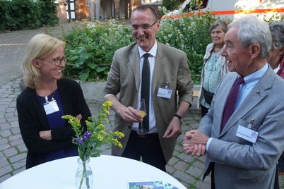 Zwei Männer und eine Frau an einem Stehtisch mit Blumen