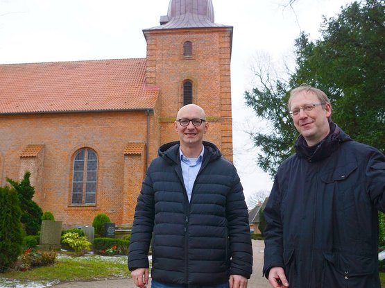 Zwei Männer in schwarzen Jacken stehen vor einer Kirche