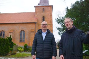 Zwei Männer in schwarzen Jacken stehen vor einer Kirche