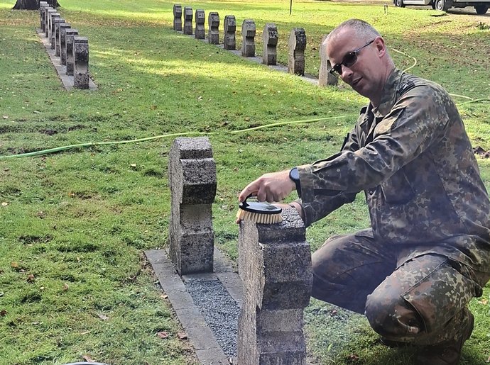 Soldat kniet und reinigt ein Grabkreuz aus Stein.