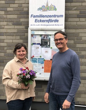 Ein Mann und eine Frau mit Blumen in der Hand stehen vor einem Schild an einer Häuserwand