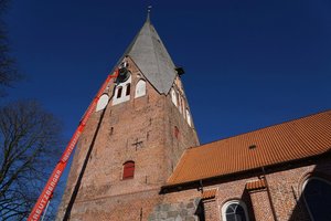 Am Kirchturm unter blauem Himmel ist ein Hubsteiger zu sehen.