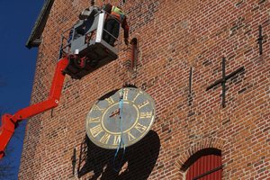 Ein Hubsteiger wird langsam herabgelassen. An einem Seil hängt das Ziffernblatt der Kirchturmuhr.