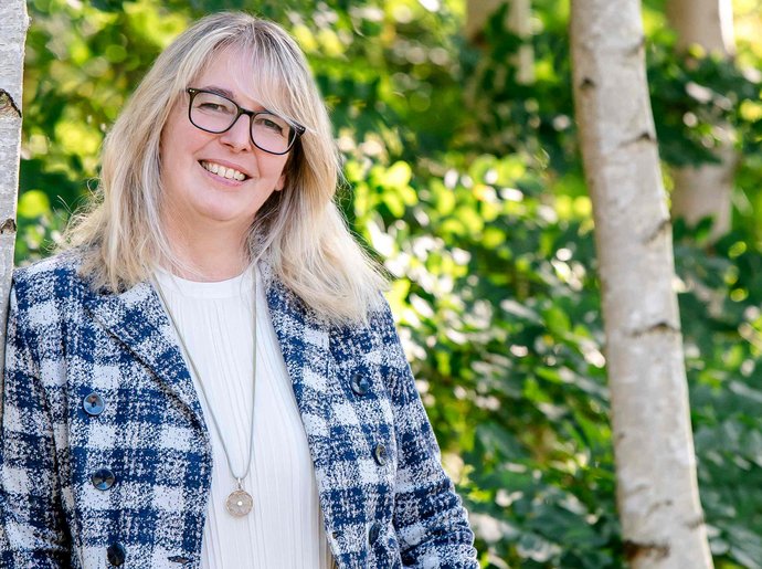 Eine Frau steht bei schönem Wetter an einen Baum gelehnt.