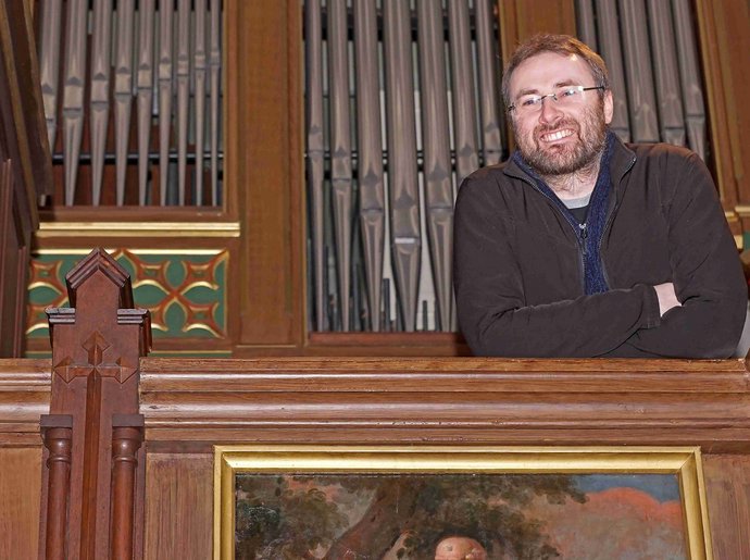 Ein Mann steht lächelnd vor einer Orgel