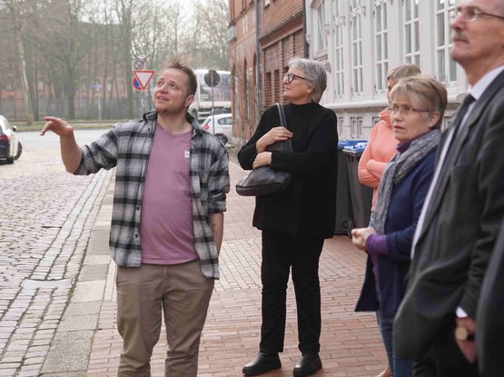 Es sind mehrere Menschen zu sehen. Ein Mann zeigt aus dem Bild heraus, die anderen schauen in diese Richtung.