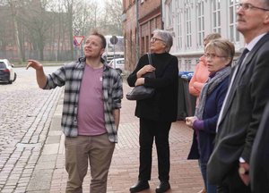 Es sind mehrere Menschen zu sehen. Ein Mann zeigt aus dem Bild heraus, die anderen schauen in diese Richtung.