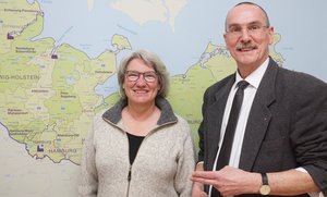 Ein Mann und eine Frau stehen vor einer Karte Schleswig-Holsteins