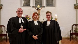 Drei Menschen im Talar vor dem Altar